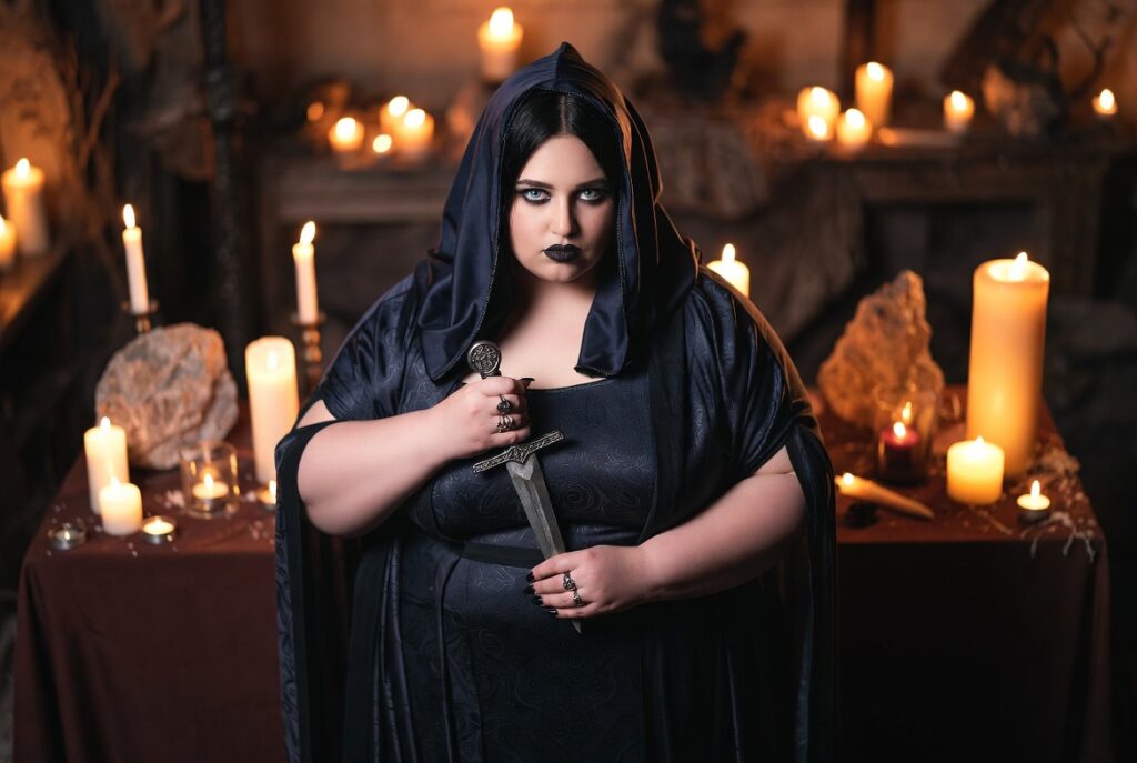 Strega esoterica in abito scuro con pugnale rituale, circondata da candele accese durante un rituale magico.